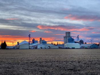 Factory on field against sky during sunset