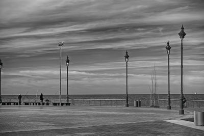 Street lights on footpath by sea against sky