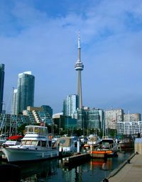 Boats moored on harbor by cityscape against sky