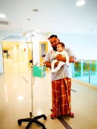 Father carrying cute daughter while standing in hospital corridor