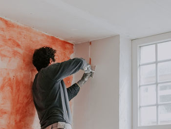 A young caucasian guy removes a construction beacon with a spatula after he puttied the wall