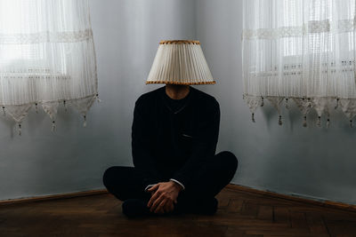 Man wearing lamp shade while sitting on floor