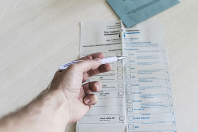 Man holding ballpoint pen over ballot paper on table