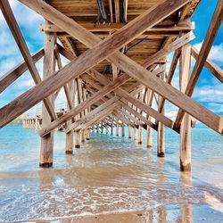 A bridge structure made of wood with a beach and sand underneath and a blue sk