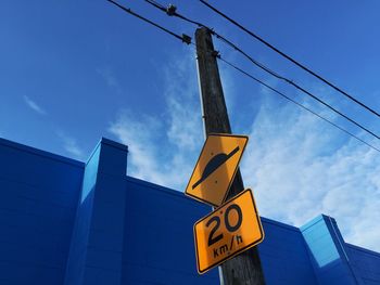 Low angle view of speed bump sign on wooden post by blue building against sky
