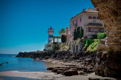 Lighthouse by houses against clear blue sky