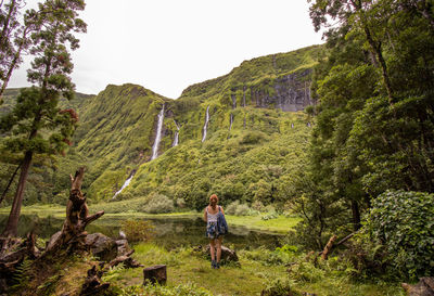 Woman in green vegetation, view to waterfall, at flores island, azores travel destination.