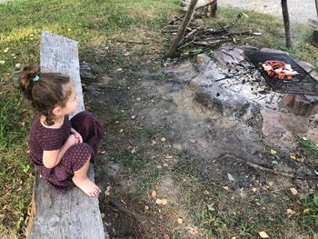 High angle view of girl sitting on wood by fire pit