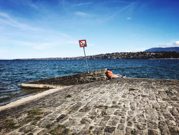 Rear view of man on rock by sea against sky