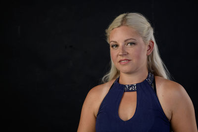 A very pretty young blonde lady in a sleeveless blue dress against a black background.