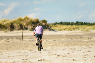 Rear view of man riding bicycle at beach