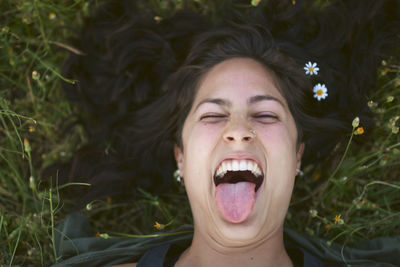 Portrait of a young woman lying in the grass with flowers in her hair. she sticks out her tongue with a happy expression