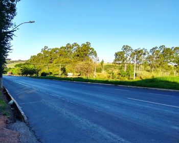 Road by trees against clear blue sky