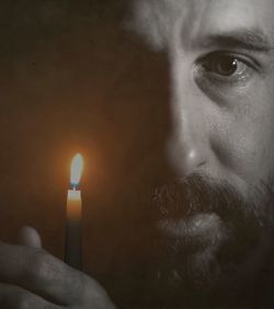 Close-up portrait of man holding lit candle