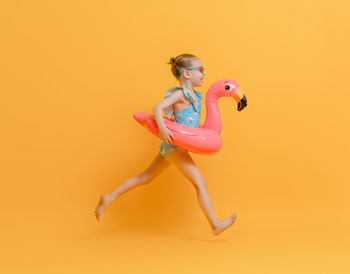 Full length of woman with arms raised against yellow background