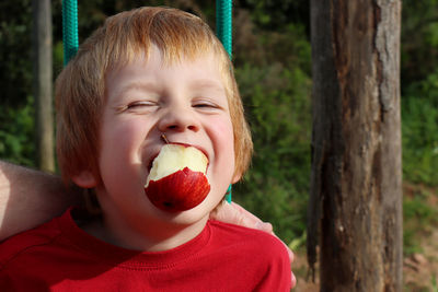 The blond narrowed his eyes and holds a red apple in his mouth. naughty five year old boy