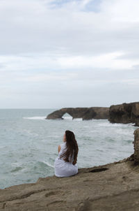 Rear view of woman sitting on beach against sky