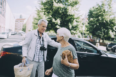 Senior male and female tourist talking while standing against car in city