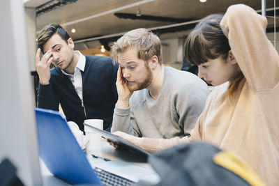 Stressed computer programmers using digital tablet at desk in office