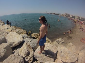 Rear view of shirtless man standing on beach against clear sky