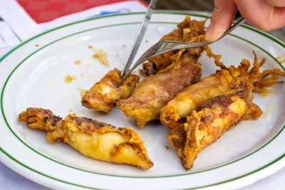 Cropped image of hand cutting fried squids in plate