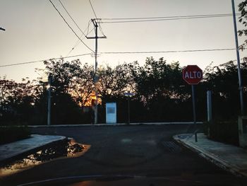 Road sign by trees against sky in city