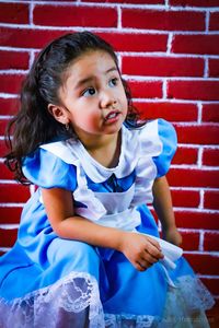 Cute girl looking away while sitting against brick wall