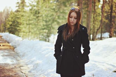 Thoughtful woman wearing winter coat standing by snow at forest