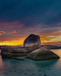 Rocks on sea shore against sky during sunset