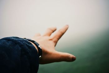 Cropped image of person hand against sky during foggy weather