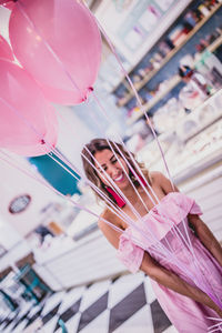 Happy woman holding pink helium balloons while standing in store