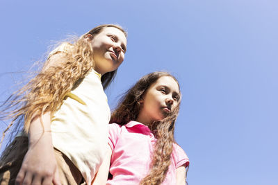 Portrait smiling two pretty sisters with extra long hair, blue sky on background, sunny day, copy