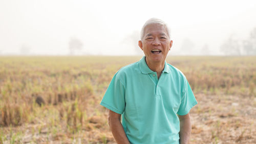 Portrait of senior man laughing while standing on field