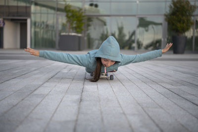 Girl with arms outstretched skateboarding on footpath