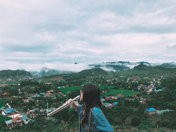 Side view of woman holding pipe with landscape in background against cloudy sky