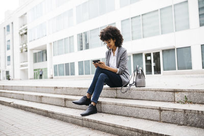 Smiling woman sitting on stairs outdoors using cell phone