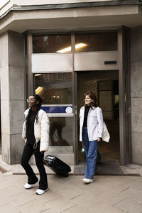 Smiling female friends leaving with luggage from hotel