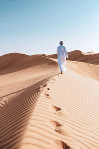 Man on sand dune in desert against clear sky