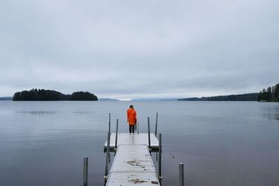 Rear view of man standing on pier over lake against sky