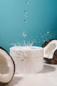 Two halves of coconut and a jar of cosmetics on a blue background with water drops.