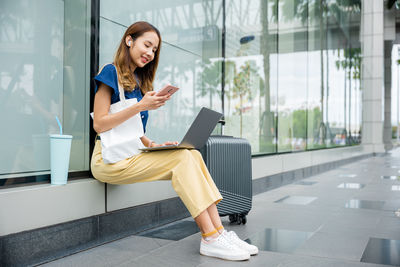 Young woman using mobile phone while sitting in city