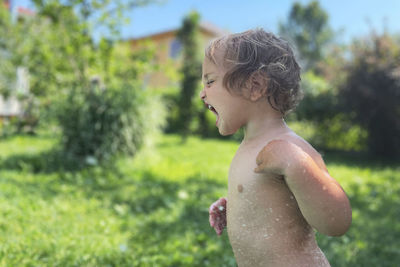 Side view of shirtless boy looking at plants