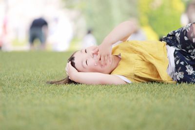 Happy girl covering face while lying on grassy field