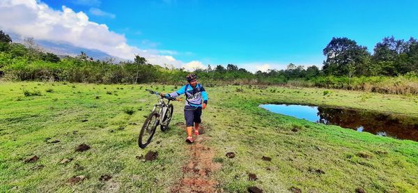 Man with bicycle on grass against sky