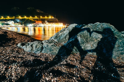 Illuminated city by sea against sky at night