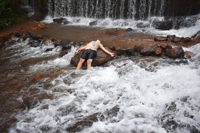 Full length of boy splashing water in waterfall