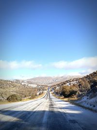 Road amidst snow covered landscape against sky