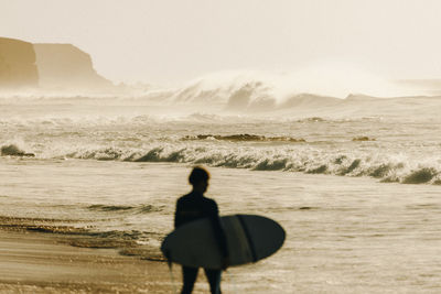 Rear view of surfer walking at beach