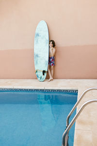 Pre-adolescent boy standing with surfboard at poolside