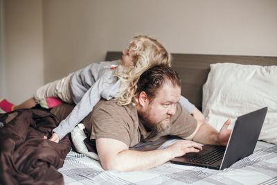 Work from home with kids children. father working on laptop in bedroom with child on his back 